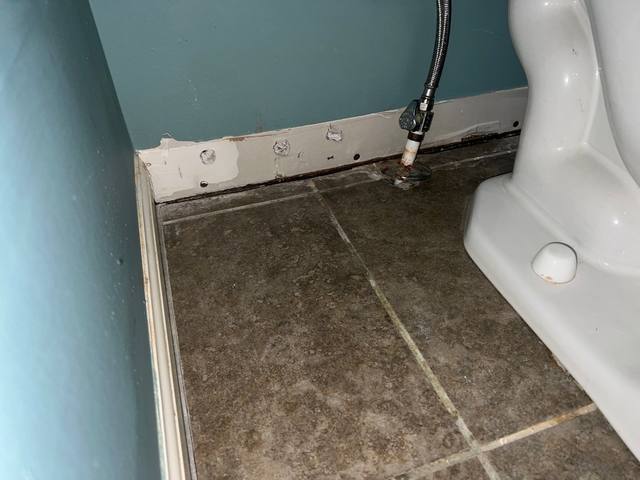 Bathroom baseboards removed so the wall can dry after an upstairs supply line leak in Lee’s Summit, MO